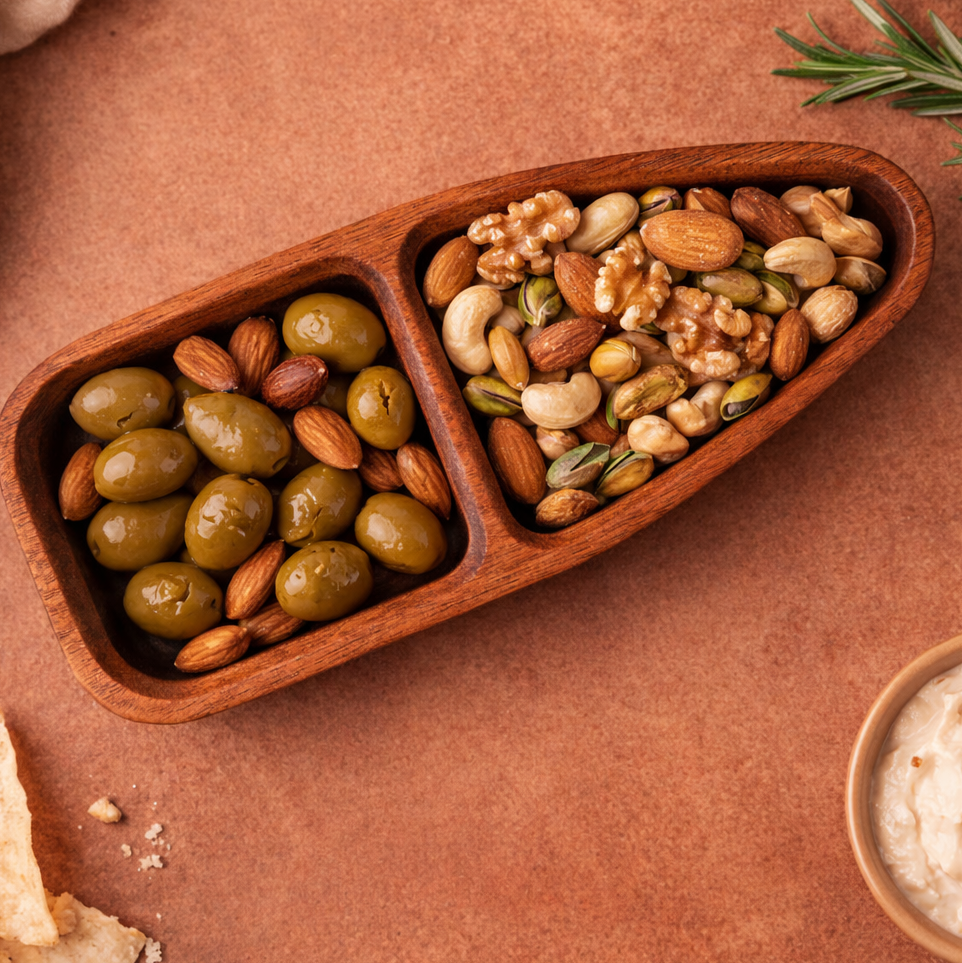 Wooden tray with compartments filled with olives and nuts on a brown surface
