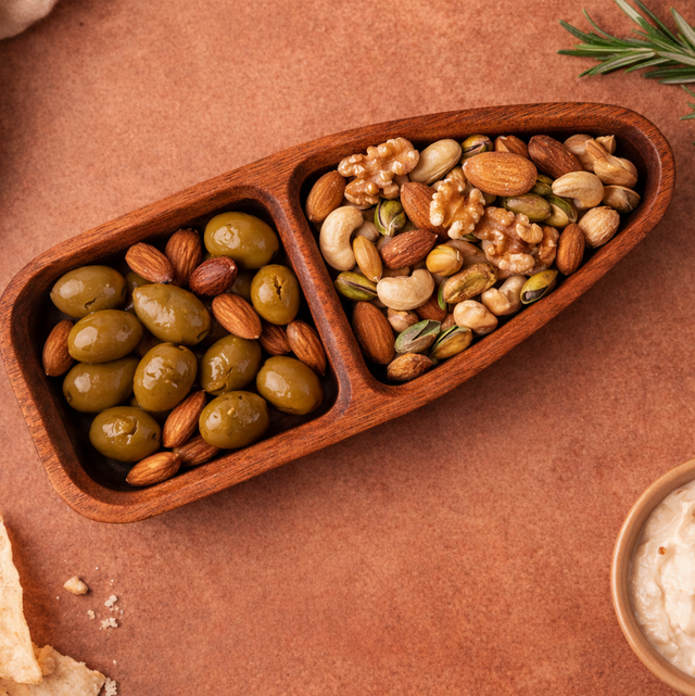 Wooden tray with compartments filled with olives and nuts on a brown surface