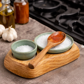 a wooden tray with ceramic bowls and wooden spoons on a kitchen counter.