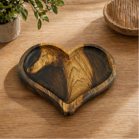 Heart-shaped wooden tray on a marble surface with a glass of water and a plant.