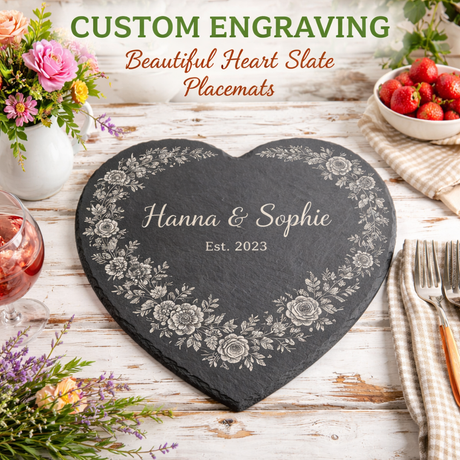 Heart-shaped slate placemat with engraved names and year, surrounded by flowers and a bowl of strawberries on a wooden table.