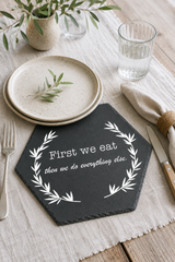 Slate placemat with 'First we eat, then we do everything else' quote on a table setting with plates and cutlery.