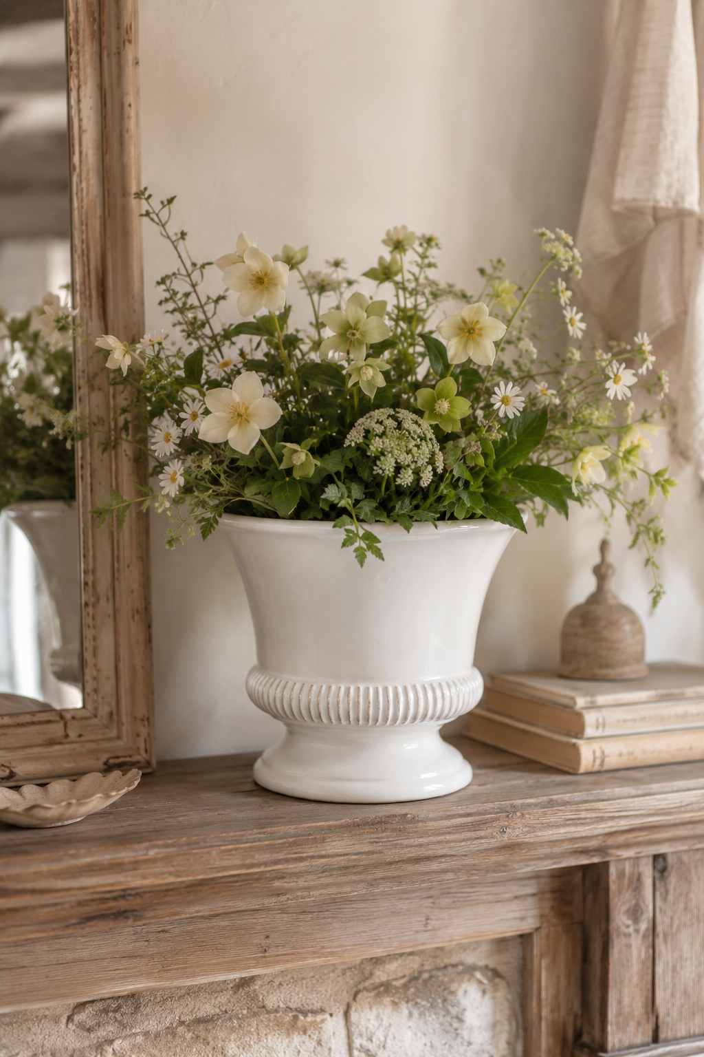 White vase with flowers on a wooden surface next to a mirror. Hinton White Ceramic Planter