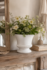 White vase with flowers on a wooden surface next to a mirror. Hinton White Ceramic Planter