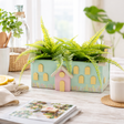 small house-shaped planters with green ferns on a wooden surface.