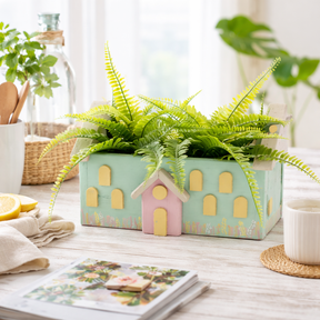 small house-shaped planters with green ferns on a wooden surface.