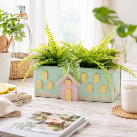 small house-shaped planters with green ferns on a wooden surface.