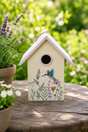 Decorative birdhouse with floral design and bird illustration on a wooden surface with plants in the background