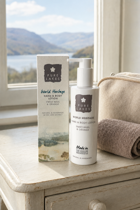 Pure Lakes World Heritage Sweet Basil & Orange Hand & Body Lotion bottle and its matching outer box, styled on a rustic white wooden table next to a beige towel, with a scenic lake and mountains in the background.