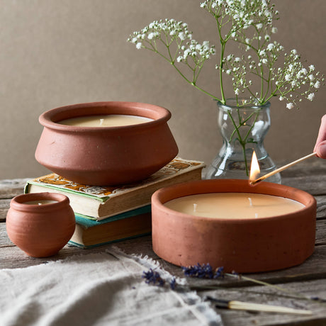 Terracotta candles on books with a vase of flowers and a lit match.
