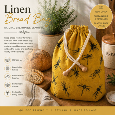 Yellow linen bread bag with dragonfly pattern on a wooden surface with bread and plants.