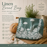 Linen bread bag with floral design on a wooden surface, accompanied by bread and plants.