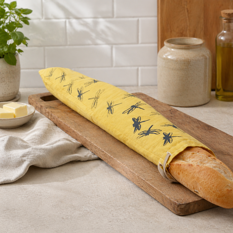 Linen bread bag covering a loaf of bread on a wooden cutting board in a kitchen setting.