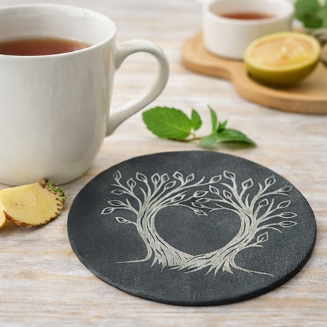 Set of four black leather coasters with tree-of-life design on a wooden surface.