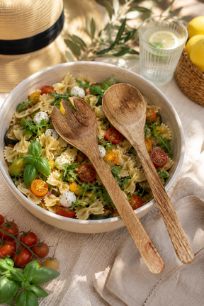Mango wood salad servers. Pasta salad with vegetables in a white bowl, set outdoors.