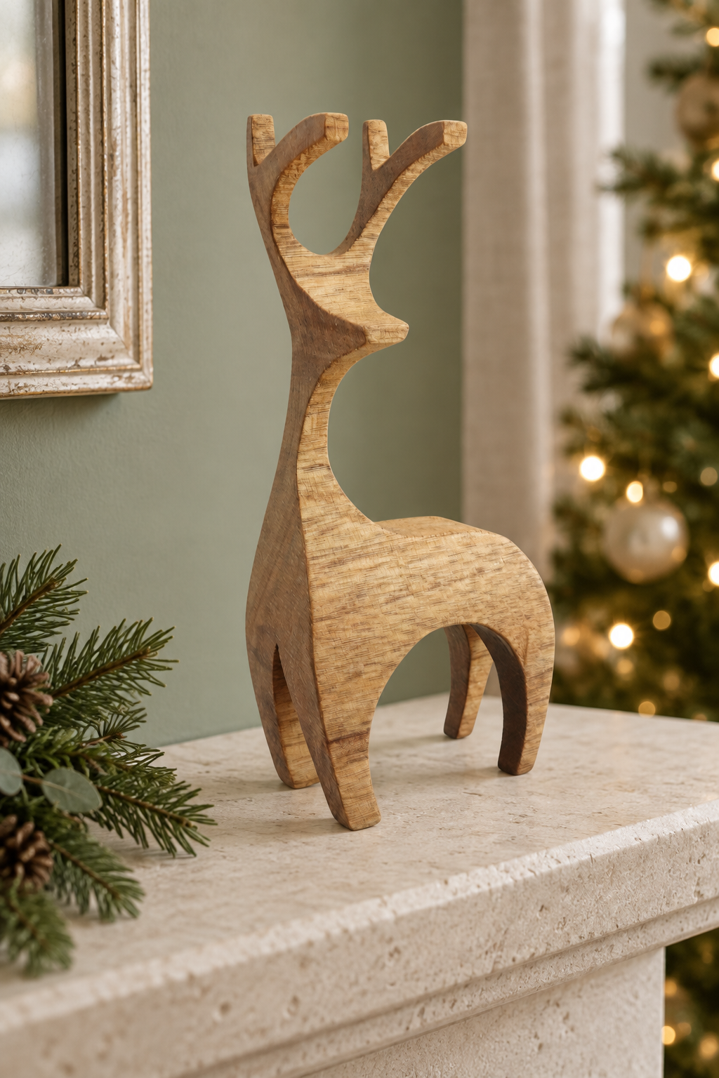 A minimalist wooden reindeer figurine with natural grain stands on a stone mantelpiece, with a blurred Christmas tree and greenery in the background.