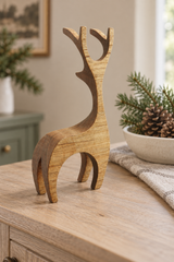 A minimalist wooden reindeer figurine with a natural wood grain finish, styled on a light wood console table next to a bowl of pinecones and evergreen branches.