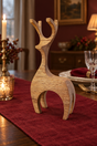 A wooden reindeer table decor sculpture with a natural wood grain finish, displayed on a red table runner in a warmly lit dining room setting.