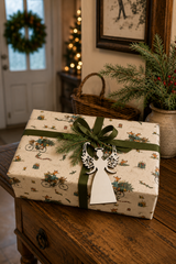 White filigree angel gift tag on a Merry Foxmas Bicycle wrapped Christmas present with green linen ribbon.