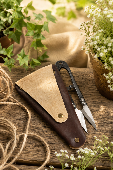 scissors sheath with a knife on a wooden surface surrounded by plants