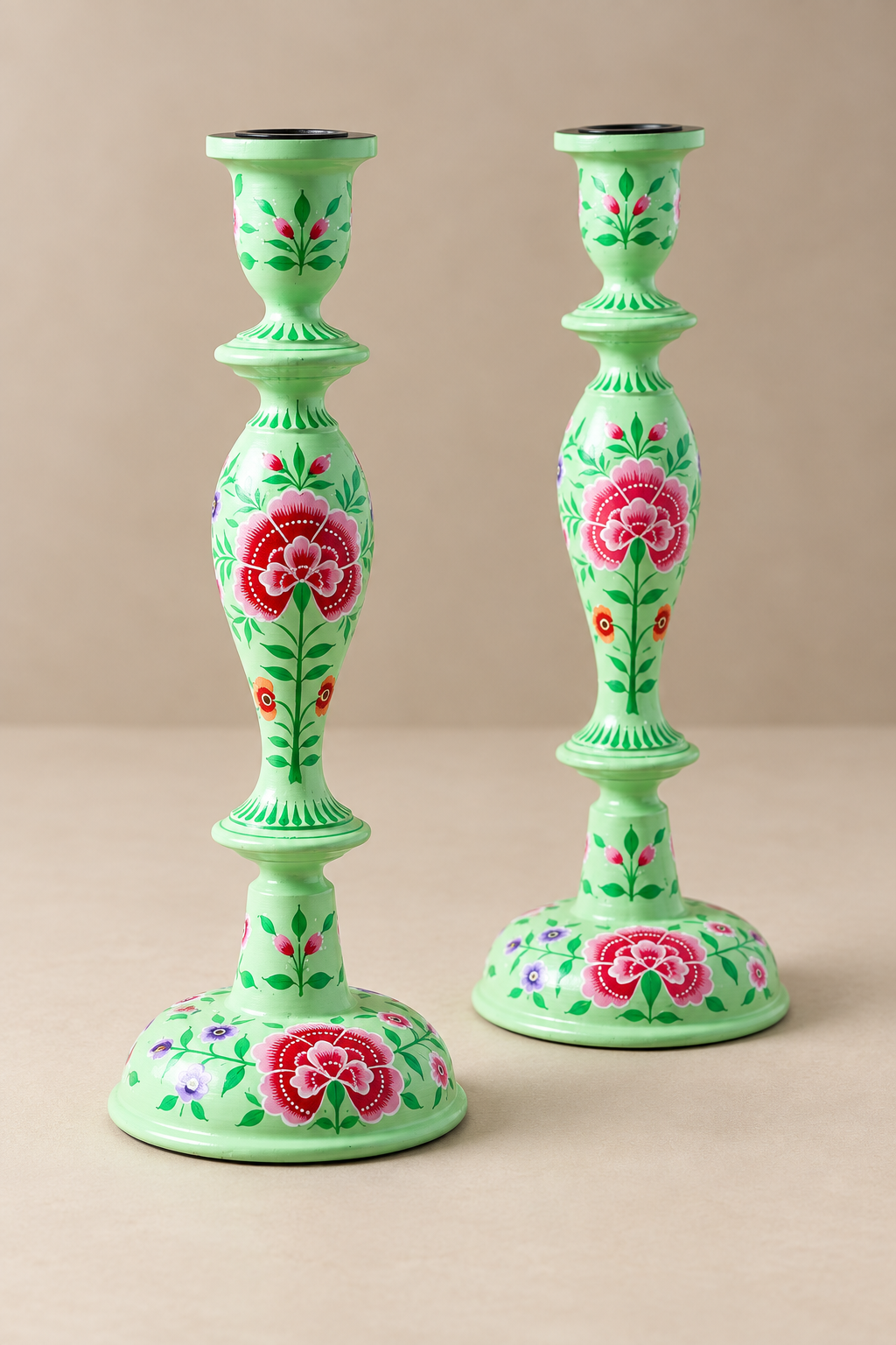 A pair of light green candlesticks decorated with hand-painted pink and red flowers and green leaves, set against a solid beige background.