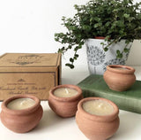 Three terracotta pots with candles on a surface, next to a box and a potted plant.