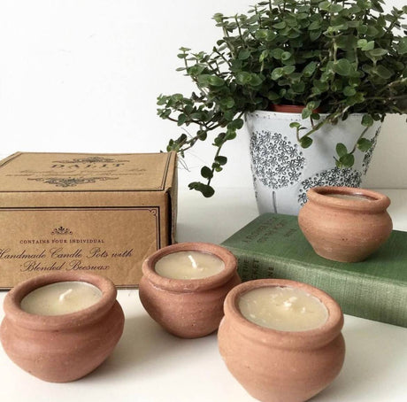 Three terracotta pots with candles on a surface, next to a box and a potted plant.
