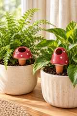 Set of two terracotta plant watering spikes with red mushroom caps, white spots and cream detailing. Includes one rounded and one taller mushroom design, each with an open filling hole and a tapered stem. Suitable for indoor pots and balcony planters.