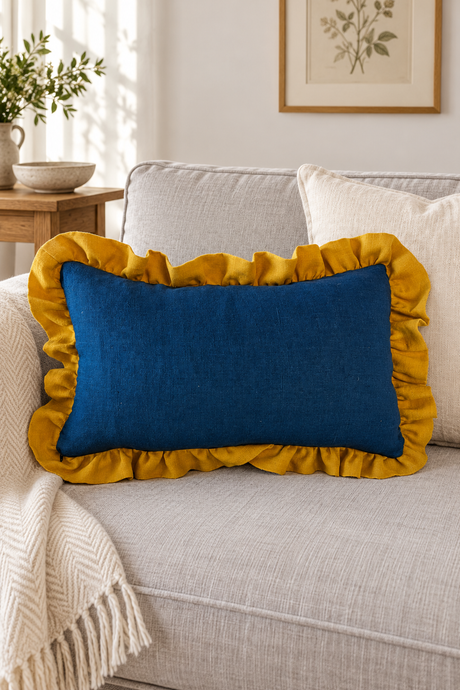 Rectangular deep blue linen cushion with a large mustard ruffle on a pale sofa beside a cream throw.