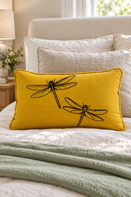 Mustard Dragonfly linen cushion, 50 × 30cm, with matching piping on ivory bedding with a pale sage throw.