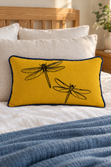 Mustard Dragonfly linen cushion with deep blue piping on ivory bedding with an oak headboard and blue throw.