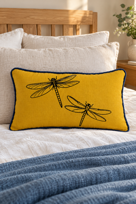Mustard Dragonfly linen cushion with deep blue piping on ivory bedding with an oak headboard and blue throw.