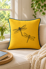 Plain mustard square cushion with blue piping against white pillows and a natural linen upholstered headboard.
