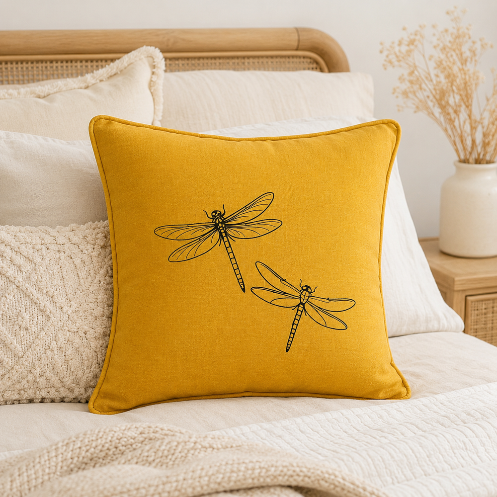 Mustard linen cushion cover with black dragonfly print, styled on a bed.