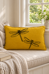 Mustard Dragonfly cushion with matching mustard piping on a cream window seat beside white flowers and a textured throw.