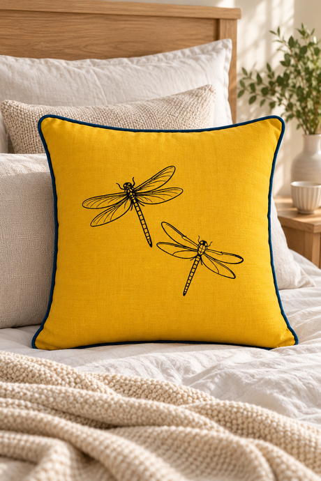 Plain mustard linen cushion, 55 × 55cm, with navy blue piping on a cream sofa with natural wood furniture behind.