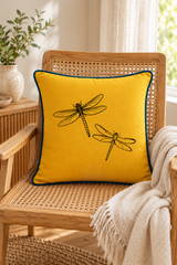 Square mustard cushion with deep blue piping on a rounded rattan armchair beside a window and cream throw.