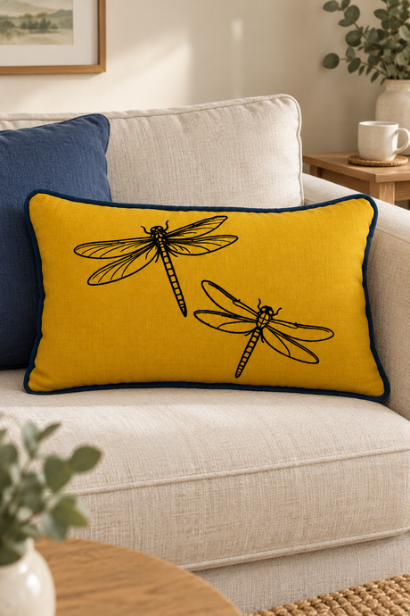 Mustard Dragonfly linen cushion, 50 × 30cm, with blue piping on a cream sofa beside a plain blue cushion.