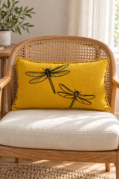 Rectangular mustard cushion with black dragonfly print and matching piping on an oak and woven cane armchair.