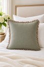 Square plain sage cushion with a small natural linen ruffle styled on an ivory bed.
