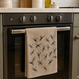 Natural Linen tea towel with black dragonfly patterns hanging on a kitchen oven door.