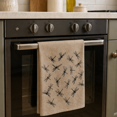 Natural Linen tea towel with black dragonfly patterns hanging on a kitchen oven door.