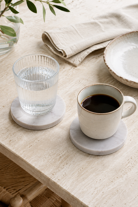 Cup of coffee and glass of water on  Natural Marble Coasters 10cm on a light wooden surface with a neutral background