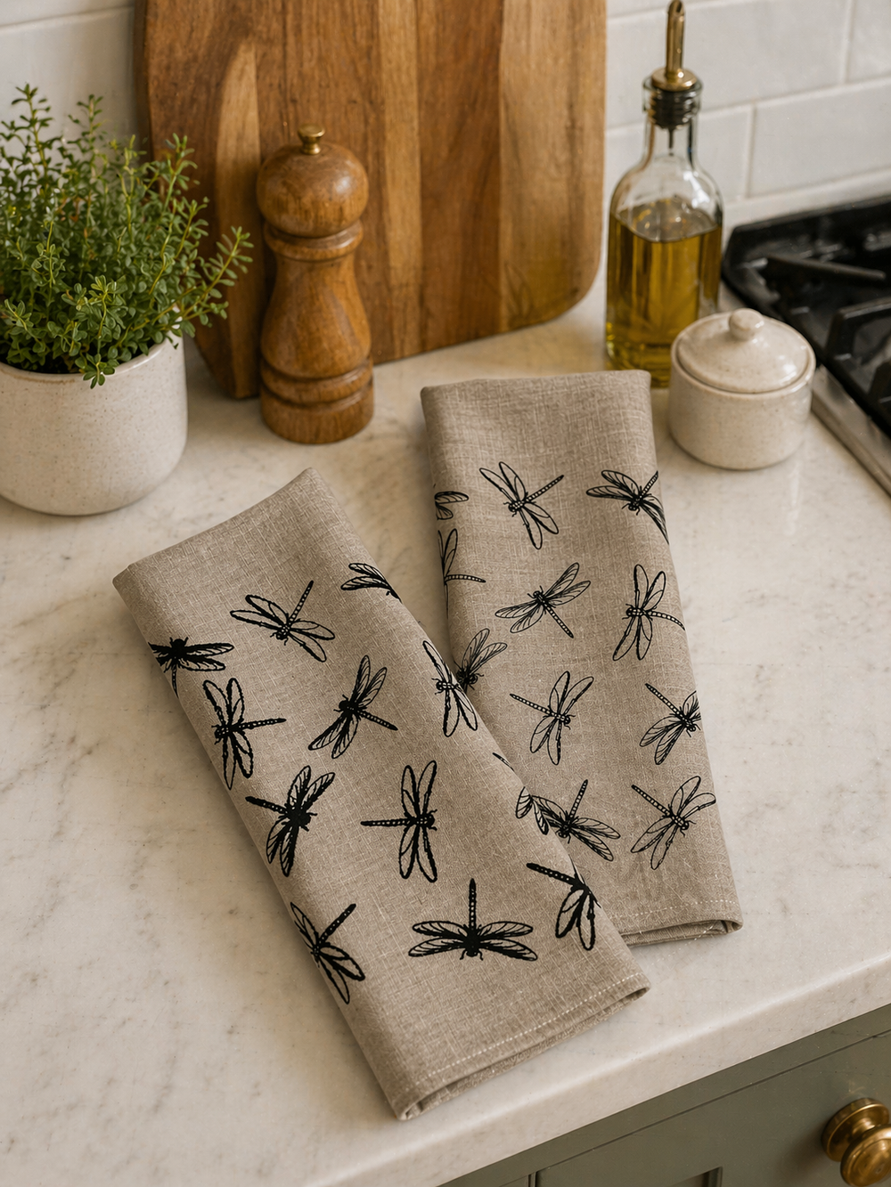 Natural line tea towels with hand printed black dragonfly patterns on a kitchen counter.