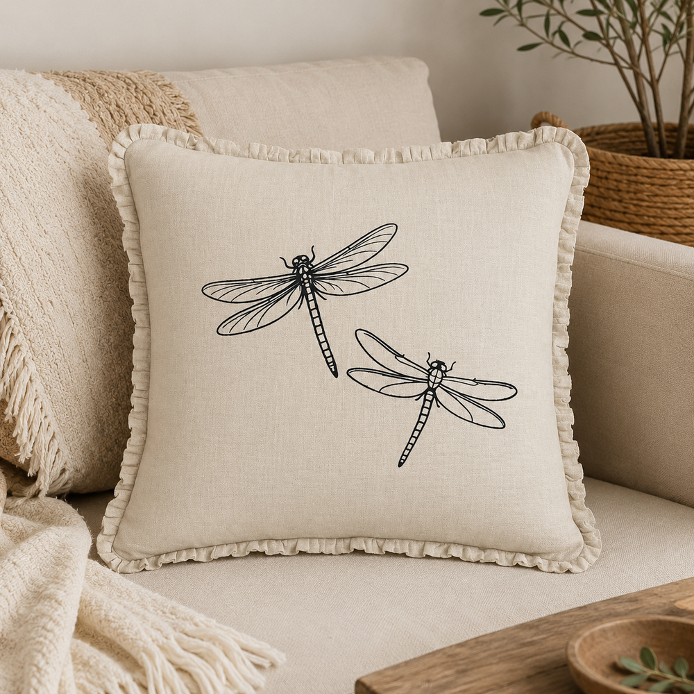 Natural linen cushion cover with black dragonfly print and ruffle edge, styled on a sofa with neutral textiles.