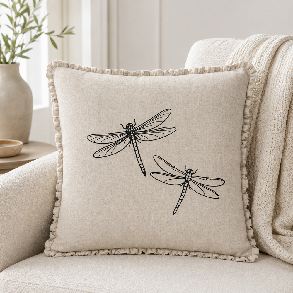 Natural linen cushion cover with black dragonfly print and ruffle edge, styled on a sofa with neutral textiles.