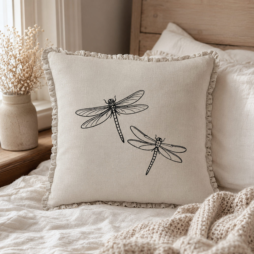 Natural linen cushion cover with black dragonfly print and ruffle edge, styled on a window seat with neutral textiles.