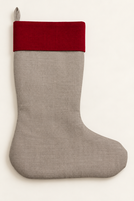 A linen Christmas stocking made of natural linen fabric with a contrasting deep red cuff, shown against a plain off-white background.
