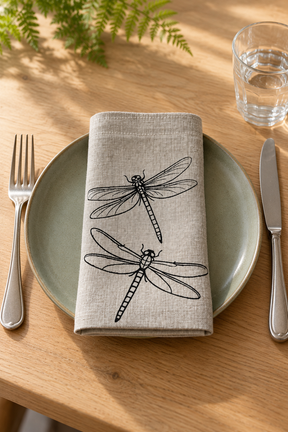 Black dragonfly linen napkin on a sage green plate, with a fork on the left and knife on the right.