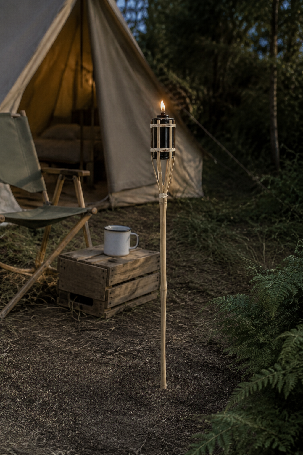A tall bamboo-torii-style outdoor torch light with a lit flame stands in a campsite setting next to a canvas tent, folding chair, wooden crate, and a white mug.